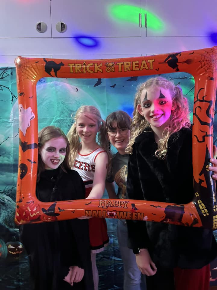This image shows 4 young people at Stagezone's Halloween Party dressed in their Halloween outfits with a trick or treat photo frame.