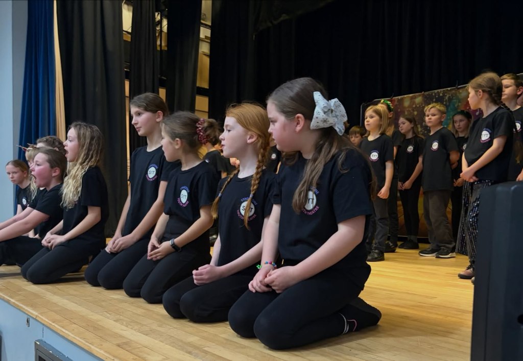 Children kneeling down performing their song at Stagezone Youth Theatre's Sparkle & Shine show